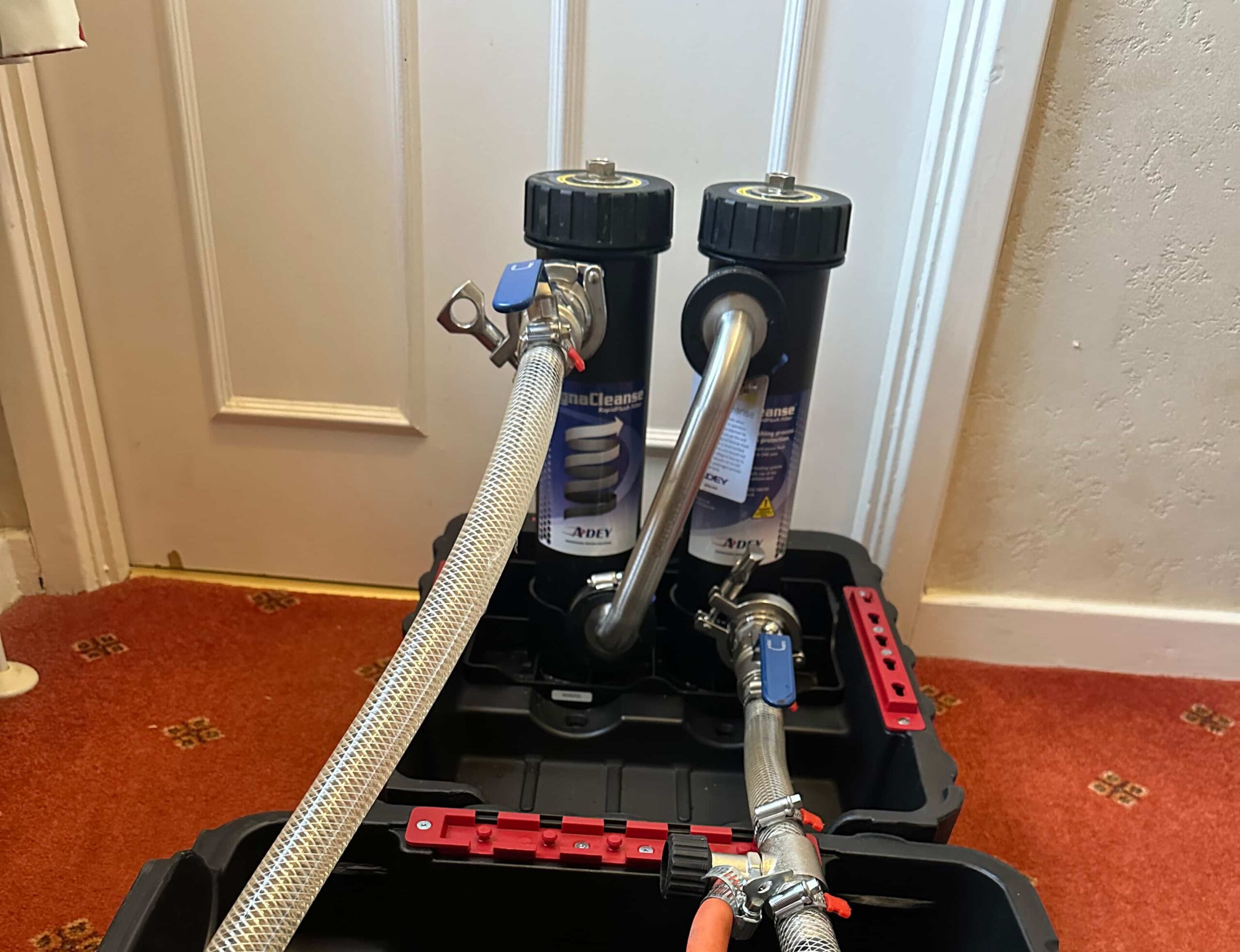 Two black cylindrical filter units with attached hoses sit on a black tray on an orange carpet.