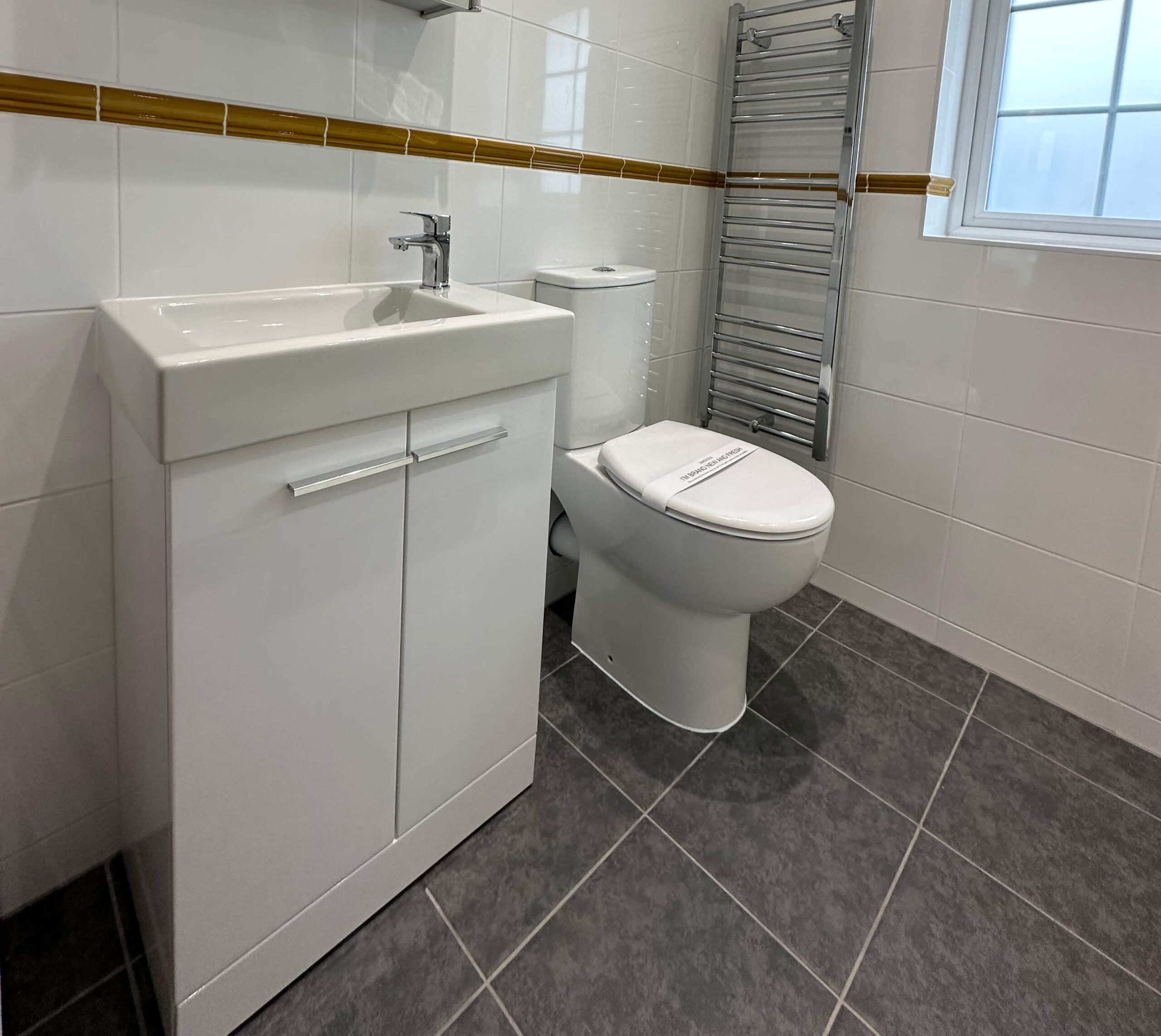 A modern bathroom with a white sink, toilet, heated towel rail, and tiled floor.