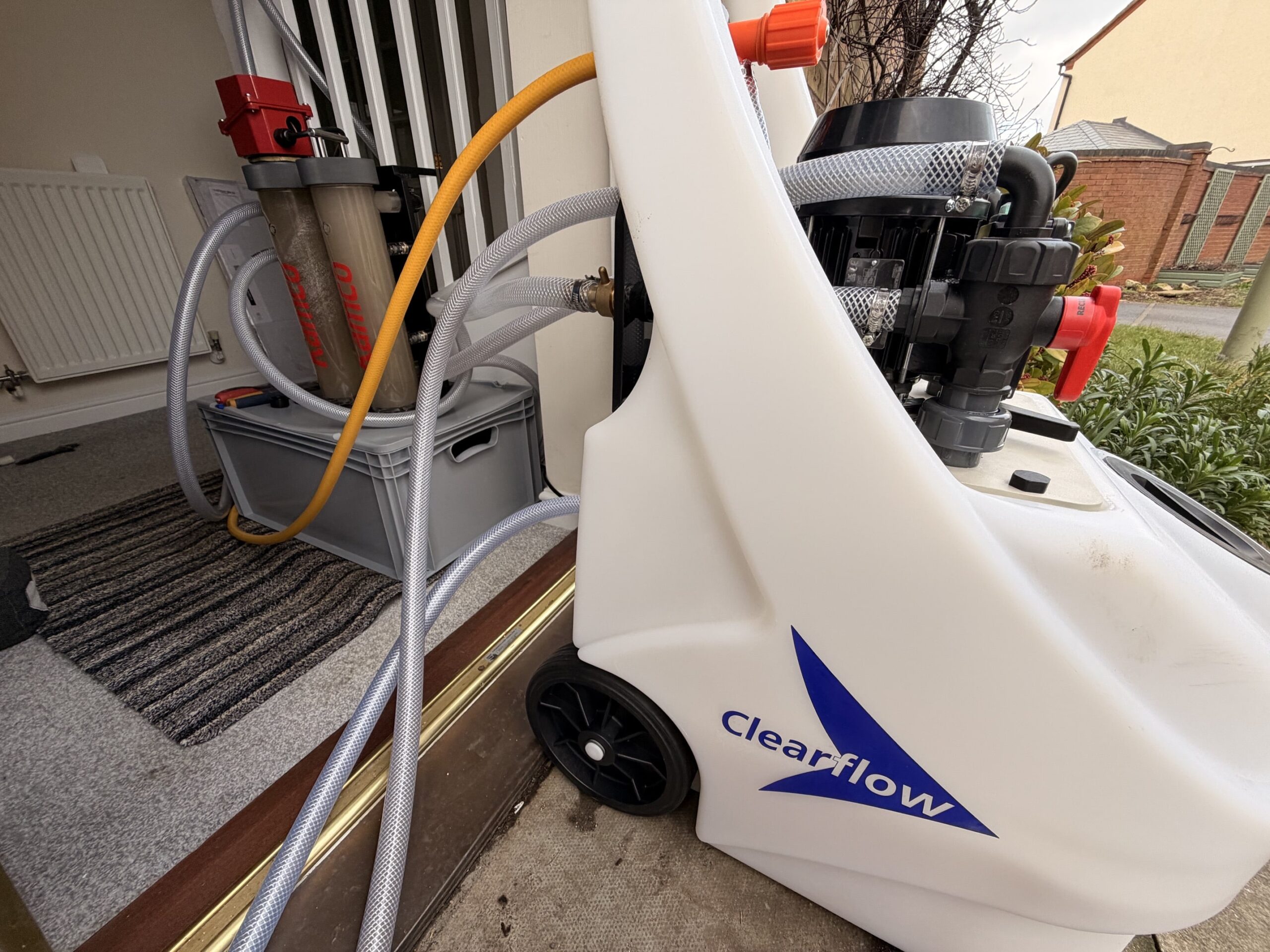 A power flushing machine connected to a heating system indoors, with tubes and a Clearflow unit.