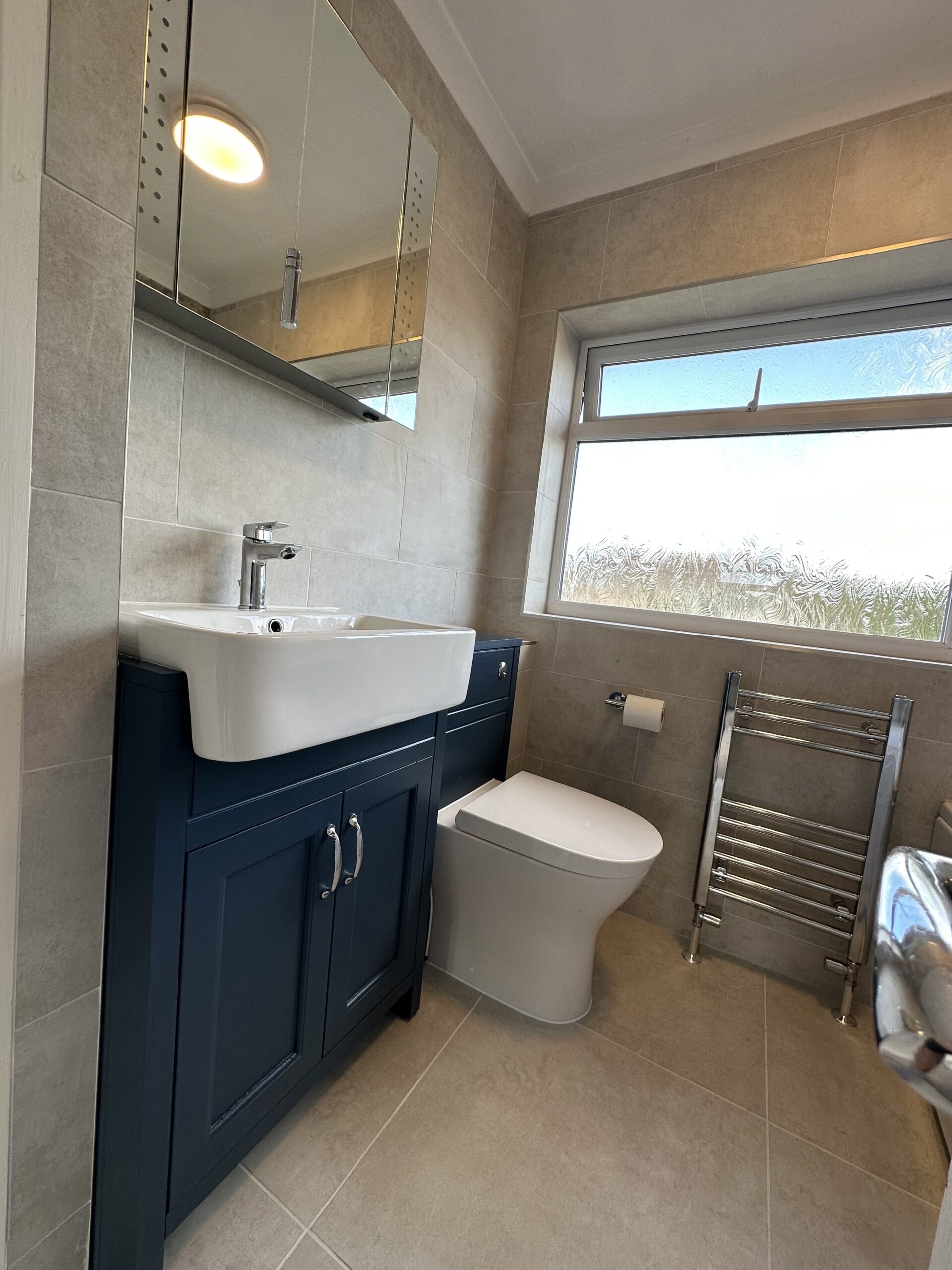 BathroomBrownTiles Modern bathroom with brown tiles, a white sink, blue cabinet, toilet, and chrome towel rack.