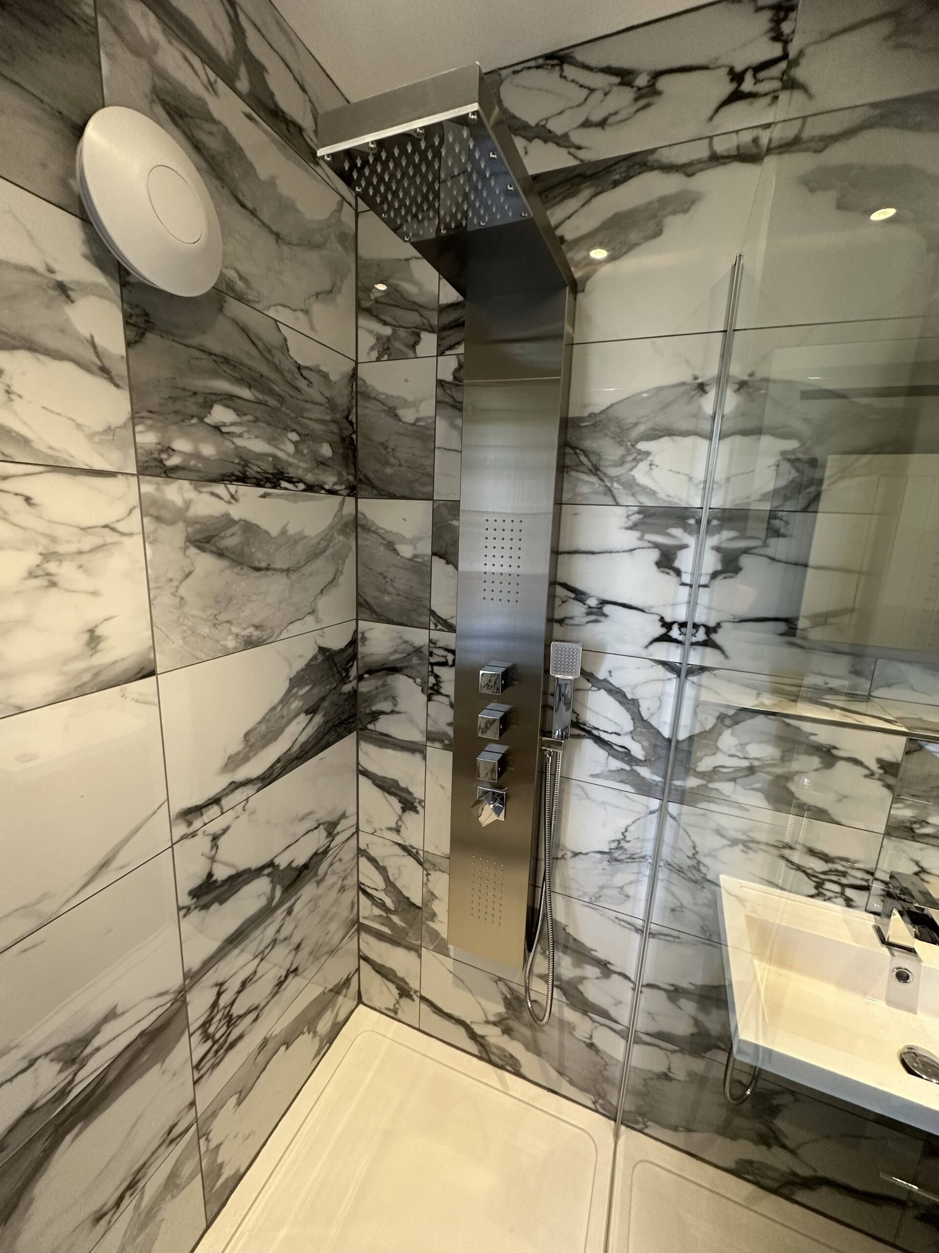 BathroomExample Modern shower with marble-patterned tiles, a rainfall shower head, and glass divider.