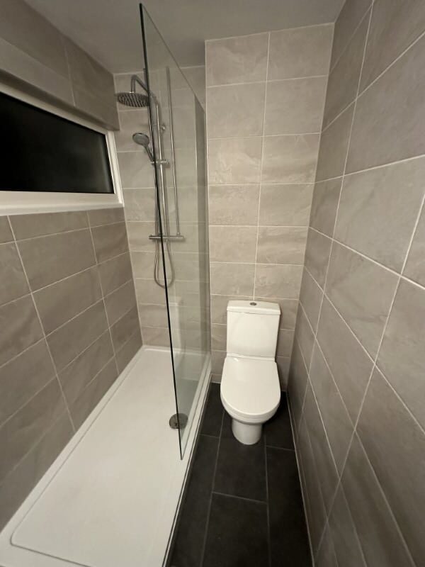 A beige-tiled bathroom with a shower on the left and a toilet on the right.