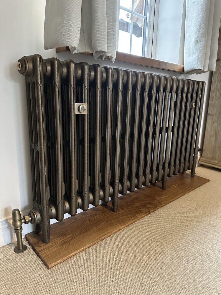 BlackRadiator A black metal radiator on a wooden base, positioned under a window with white curtains.