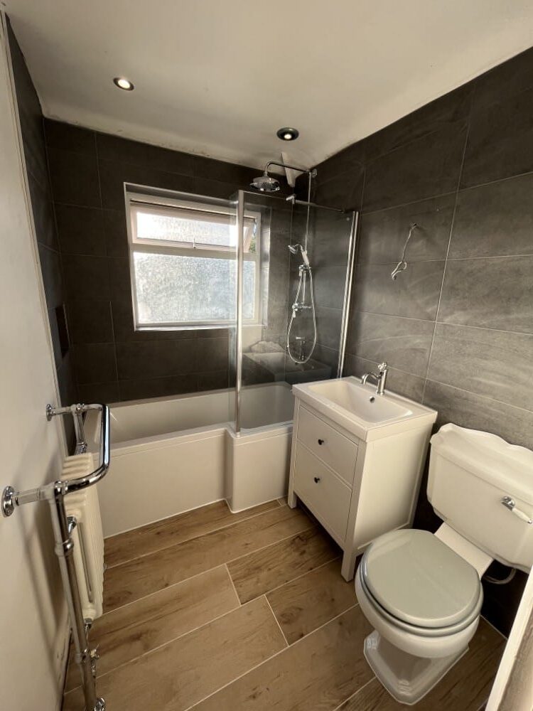 BlackTiledBathroom Small bathroom with black tiled walls, a bathtub and shower, white sink cabinet, and toilet.