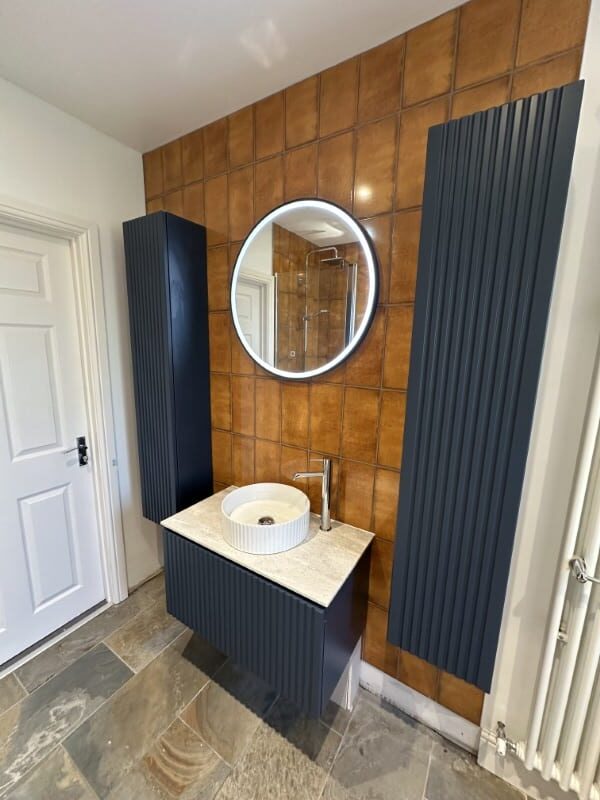 Modern bathroom with a round mirror, brown tile wall, blue vanity, and white sink.