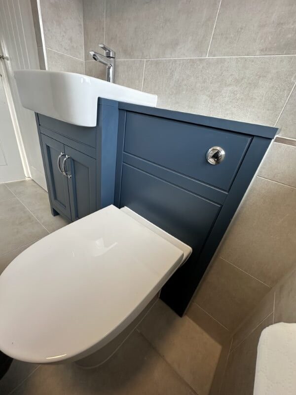 White toilet and sink next to a blue cabinet against beige tiled bathroom walls.
