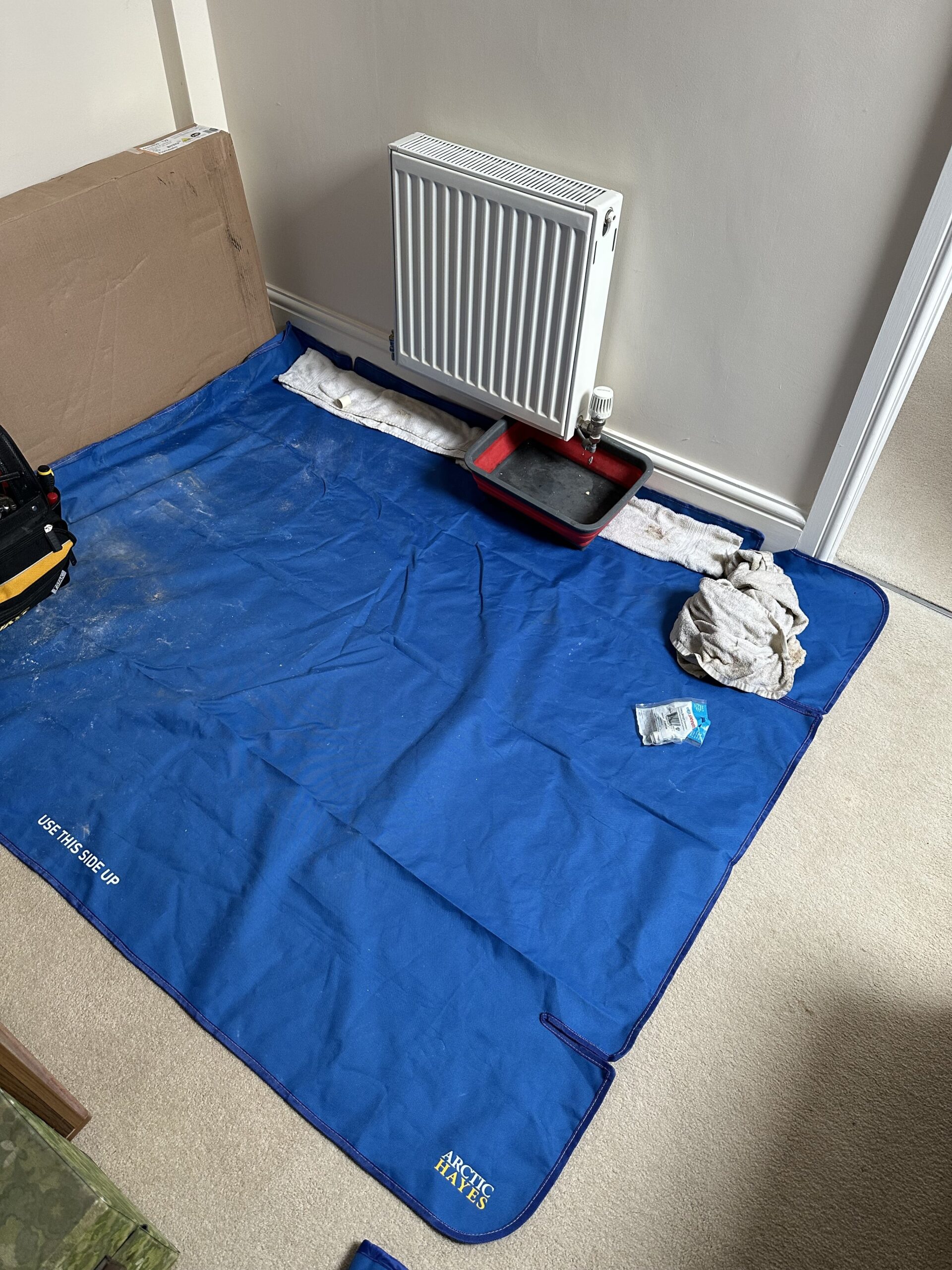 BlueMatt Blue protective mat on floor by a radiator, with tools, cloths, and a tray for catching water.