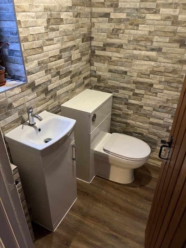 Small bathroom with brick-patterned tiles, a white toilet, and a white sink cabinet on a wood floor.