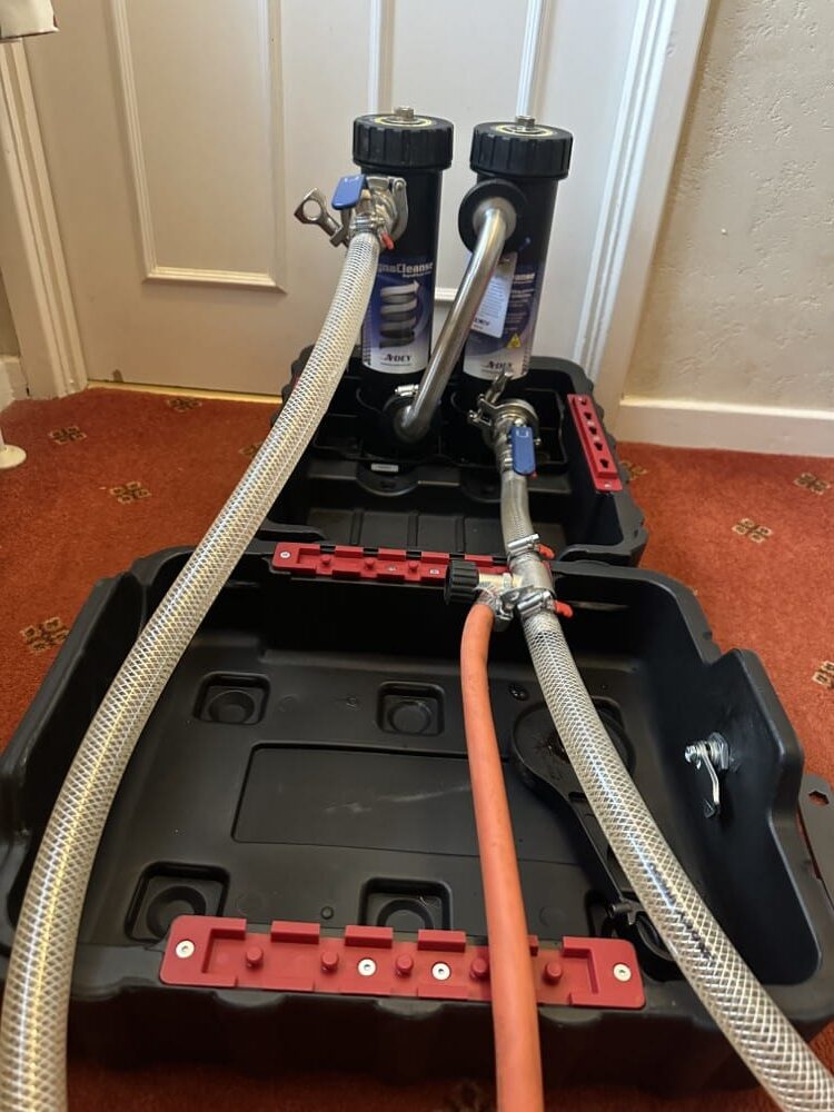 Two water filter canisters with attached hoses placed in a black plastic tray on a red carpet.