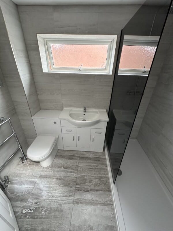 Modern bathroom with grey tiles, a white toilet, sink unit, and glass shower enclosure.