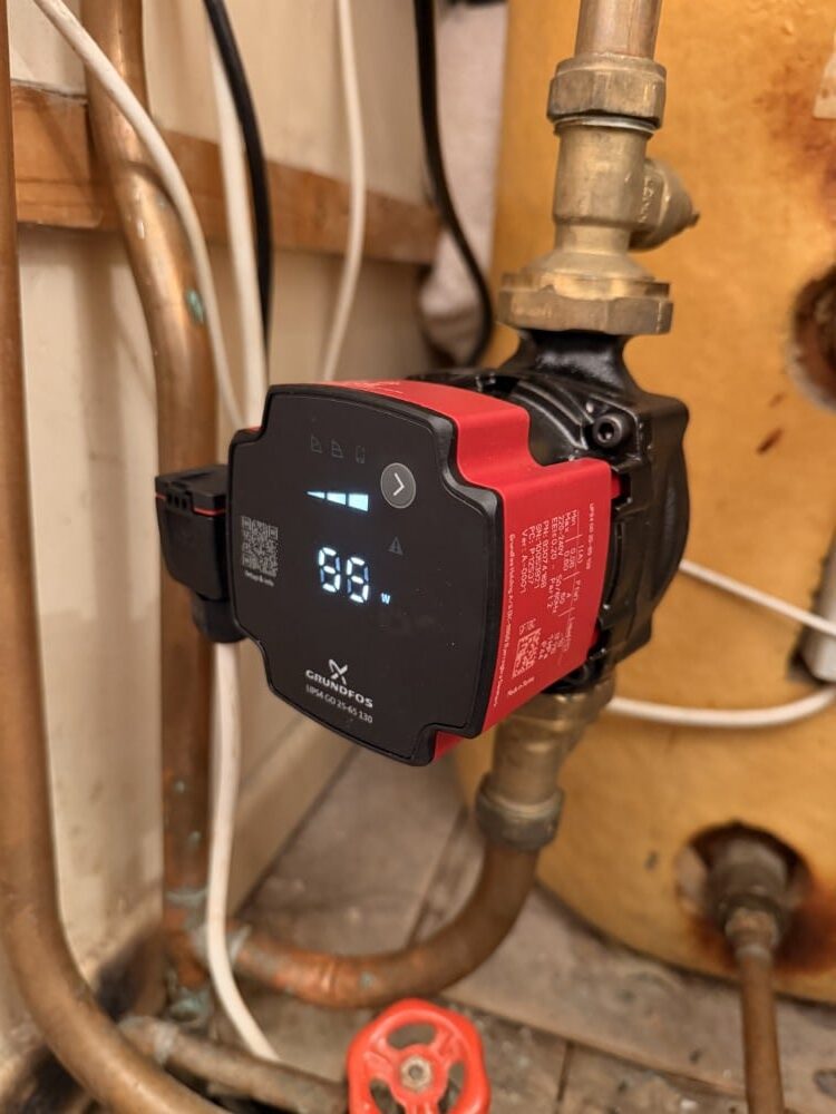 Digital heating system pump attached to pipes, displaying "88 W" on the front panel.