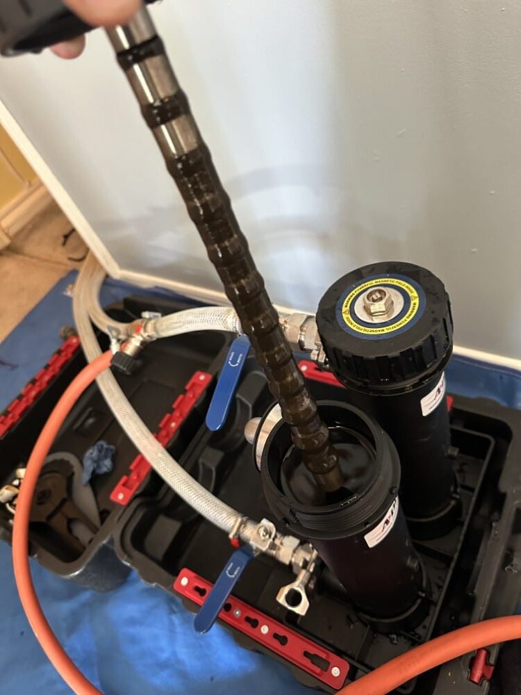 A close-up of a hand using equipment to clean or service a heat pump filter system.