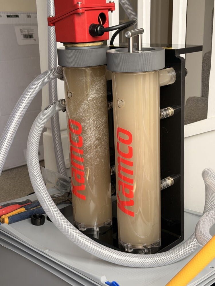 Two transparent filter cylinders connected by hoses, with cloudy water inside.