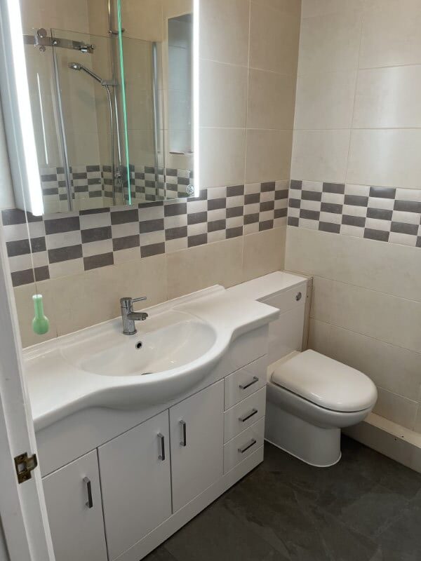Modern bathroom with a white sink, vanity drawers, toilet, mirror, and checkered wall tiles.
